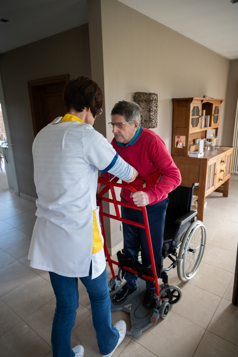 verpleegkundige helpt patiënt recht te staan uit rolstoel en draagt toestel om ergonmische houding te meten