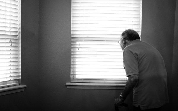 Oude man kijkt uit het raam
