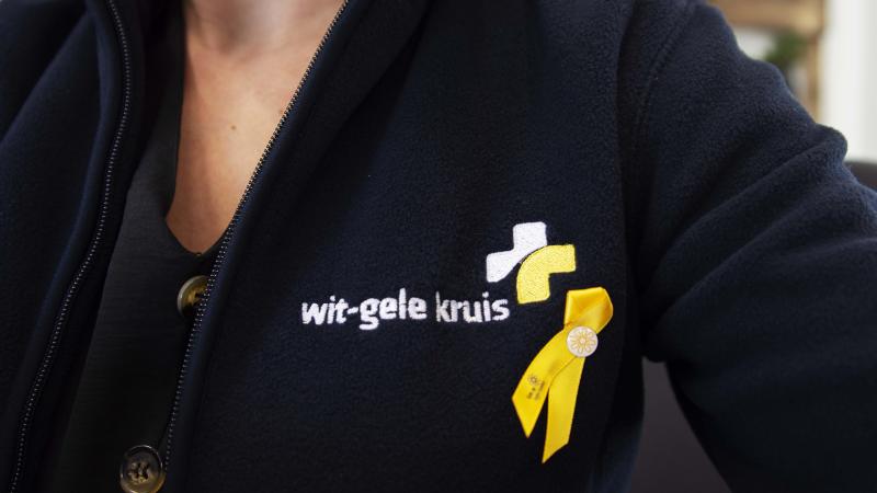 Geel lintje Kom op Tegen Kanker opgespeld bij Wit-Gele Kruis medewerker